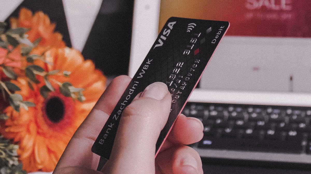 Hand holding credit card in front of laptop